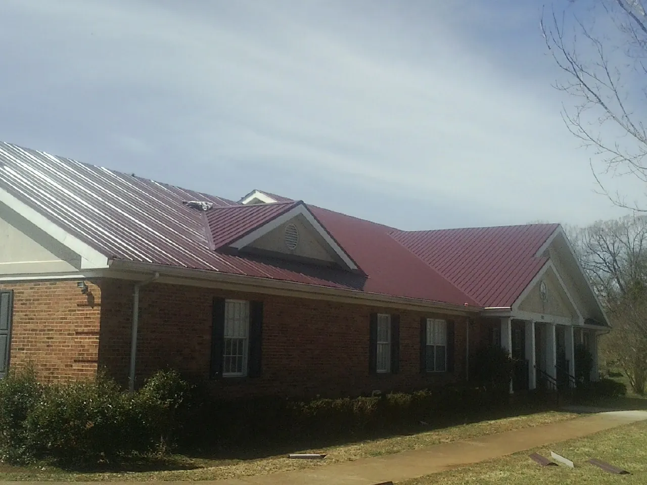 Red metal roof with gabled entries on a long brick building, from a Hail Damage Roof Repair job in Morrison