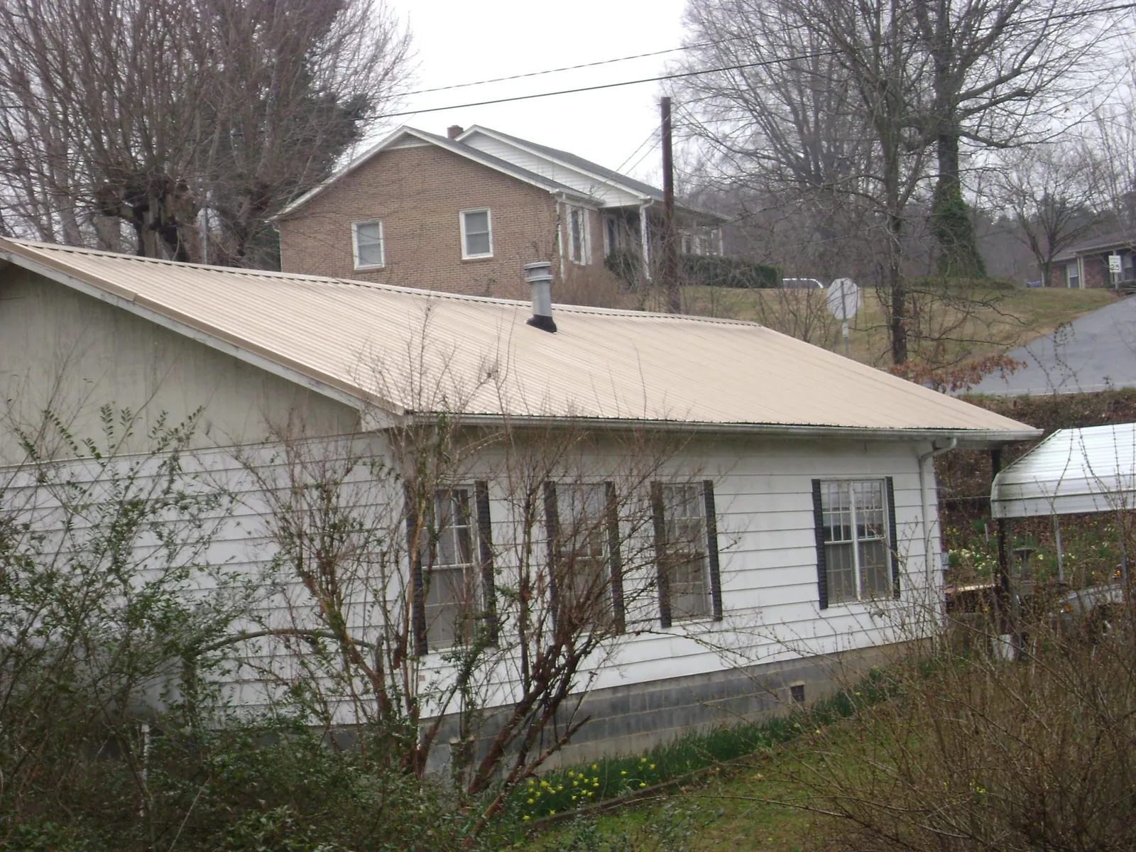 Tan metal roof on a white sided house set into a hillside — Commercial Roofing by Roofing Brothers in Morrison