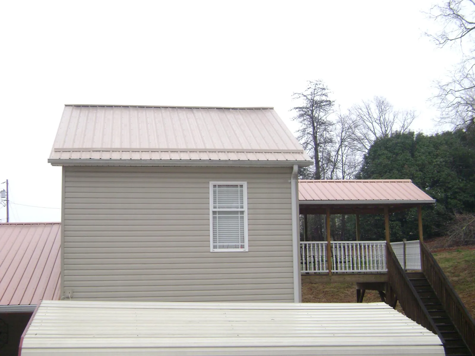 Tan metal roofs on a two story addition and attached porch, from a Roof Replacement job in Morrison